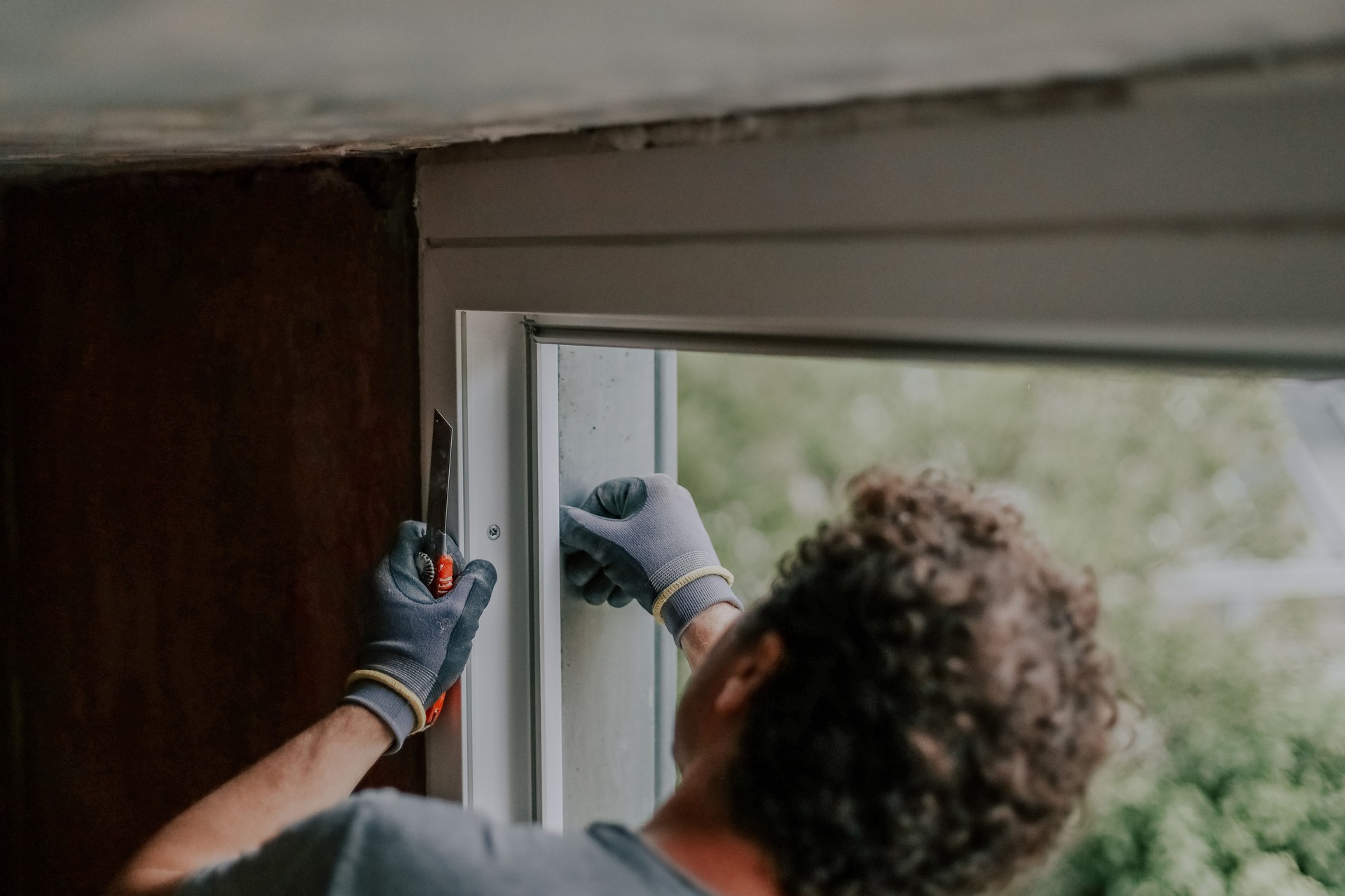 A man cleans a window frame from the outside with a construction knife.